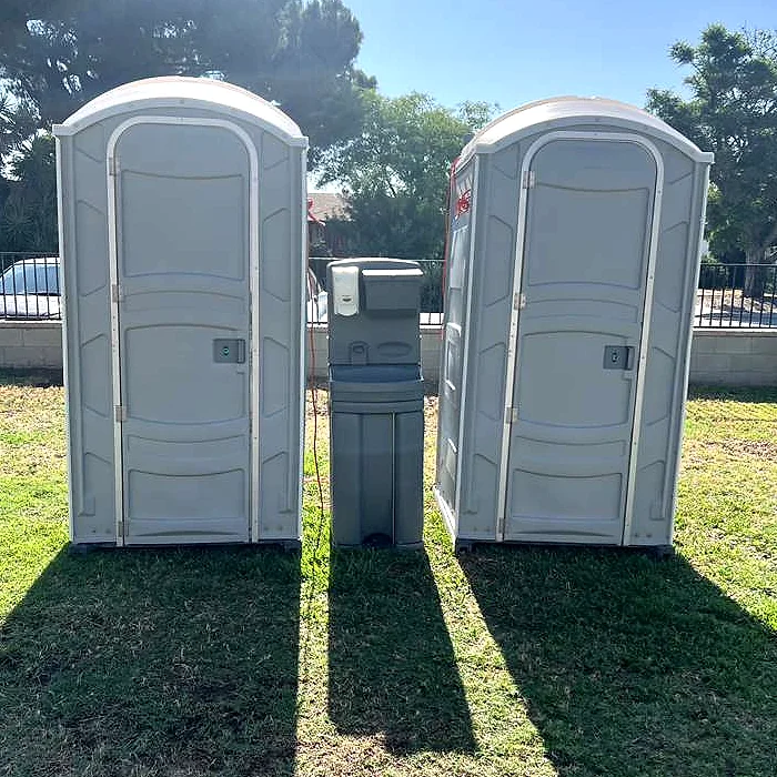 Two portable toilets with an exterior handwashing station set up together on grass